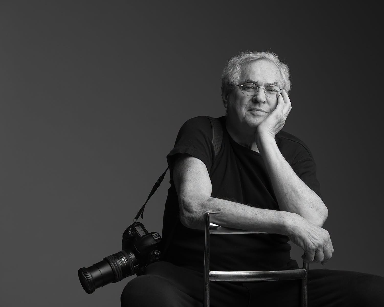 Jay Maisel seated with a camera over his shoulder, chin resting on his hand